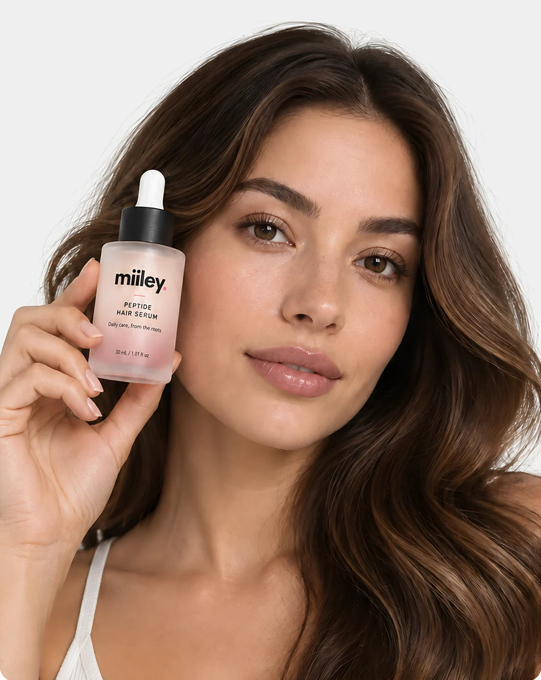 Woman holding Miiley Peptide Hair Serum next to her face